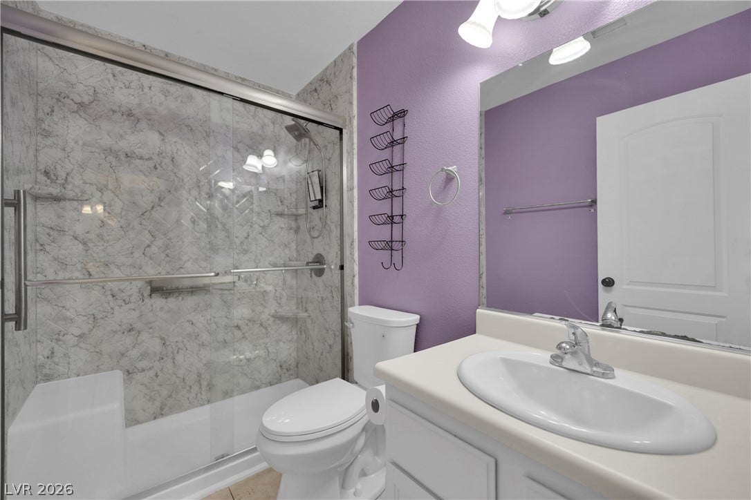 Marble patterned tiling surrounds a modern shower stall adjacent to a white vanity.