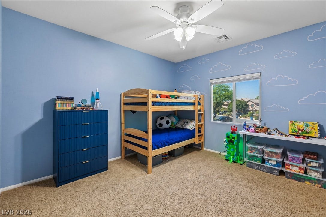 A well-lit bedroom features plush carpeting and a bright window overlooking the neighborhood.