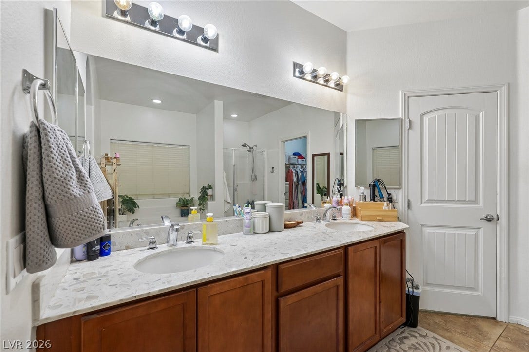 Double vanity with stone counters provides ample space and functionality in this bright primary bathroom.