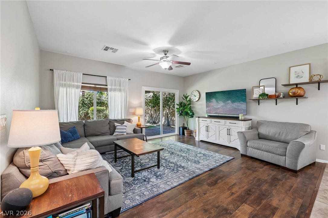 An inviting living area features warm wood flooring, a subtle ceiling fan, and direct patio access through glass sliding doors.