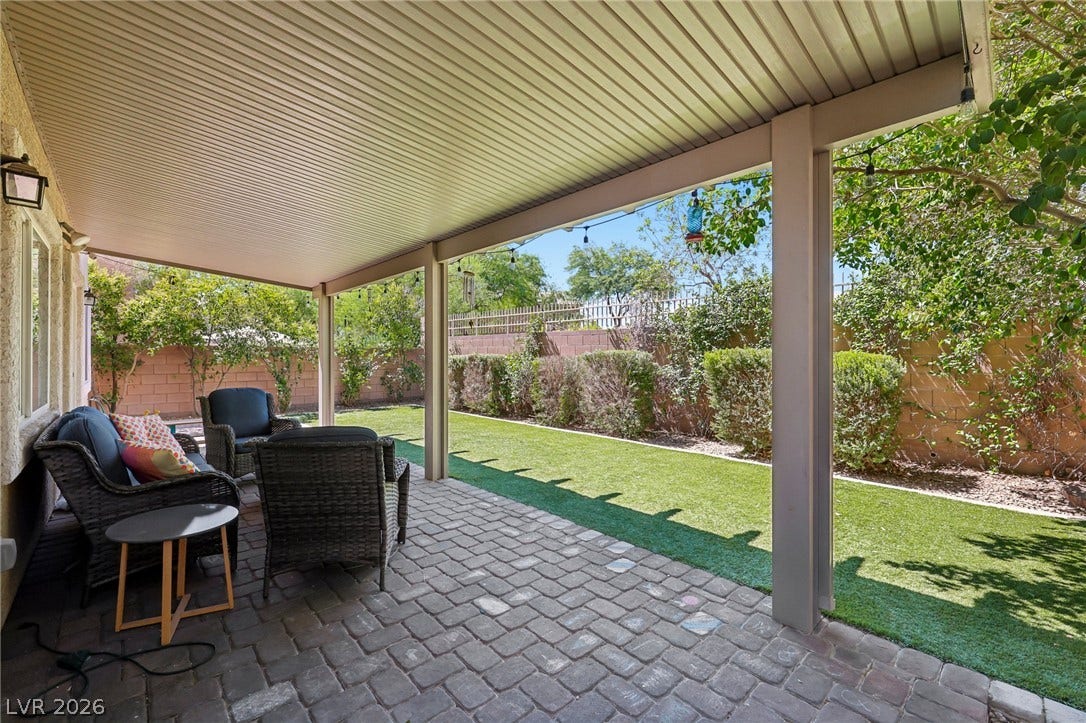 A private covered patio with paver flooring extends to a lush green yard, ideal for outdoor leisure.