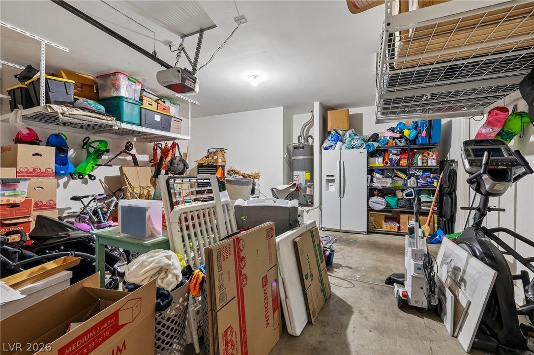 This organized garage offers extensive overhead storage racks, a water heater, and a secondary refrigerator.