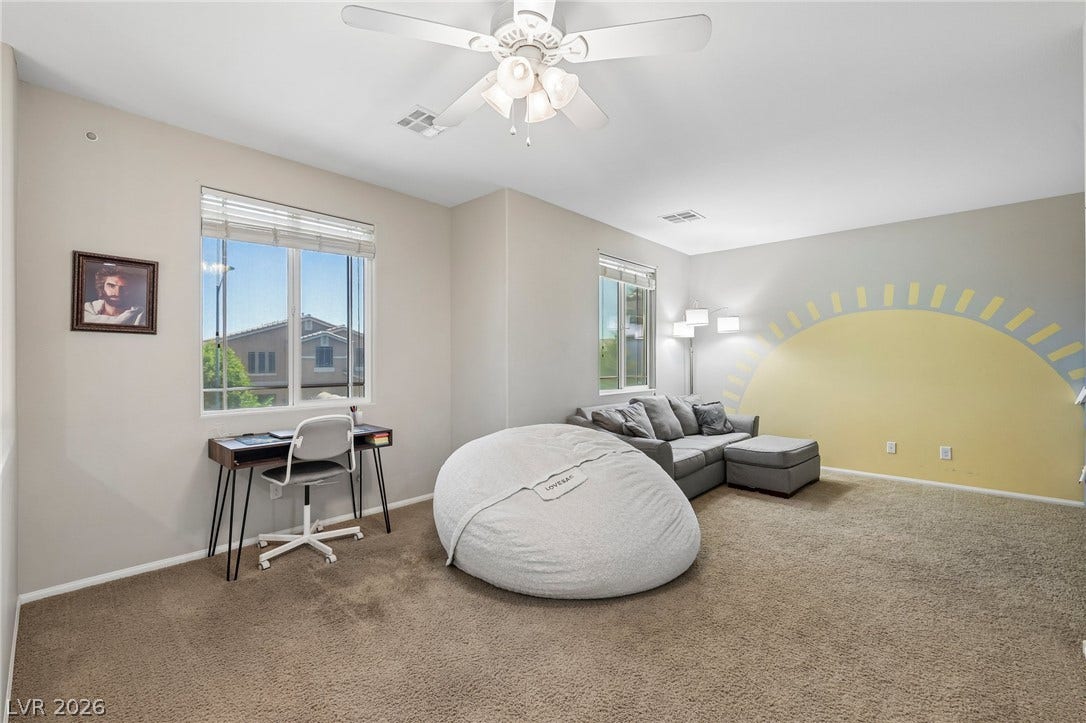 A well-lit bedroom features plush carpeting, bright windows, and a convenient ceiling fan.