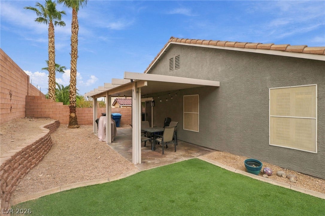 A covered patio shades the concrete lounge space next to a tidy back lawn.