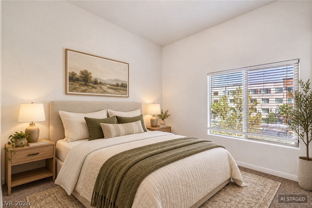 A wide window illuminates this bedroom space, highlighting the high ceiling and plush carpeting.