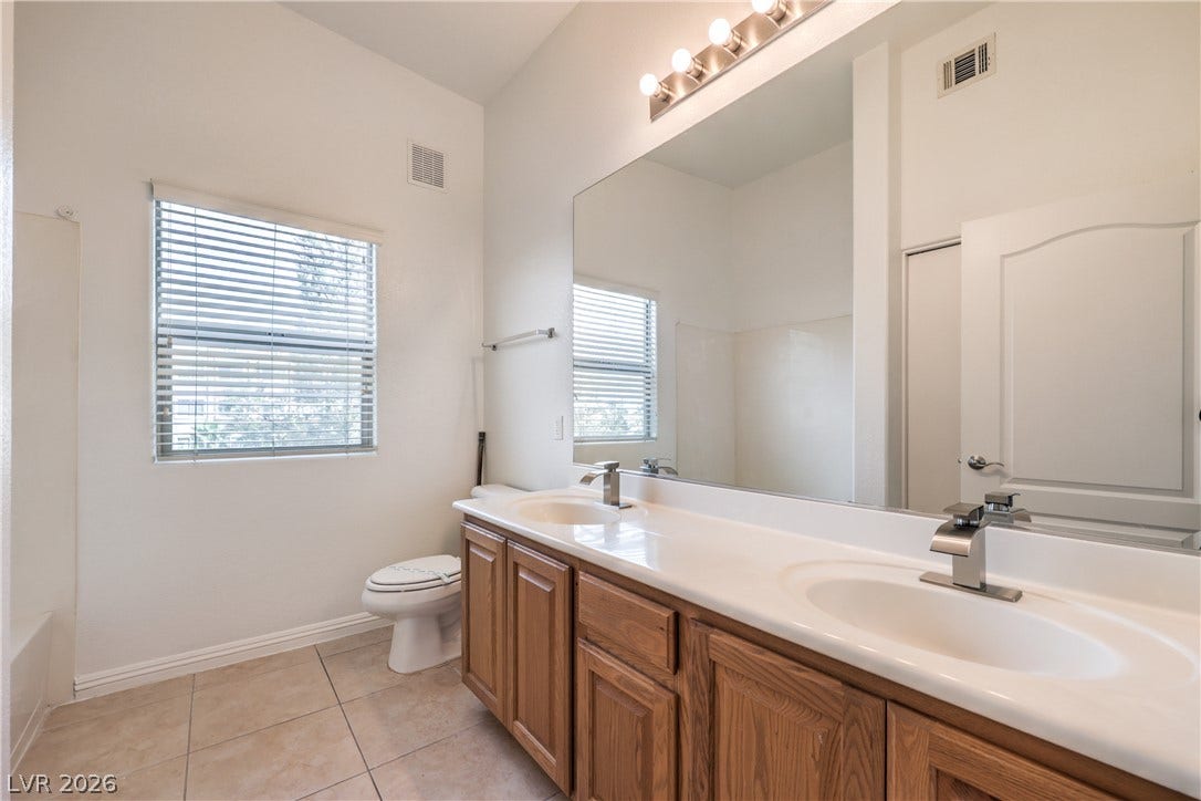 Tile flooring and a long vanity with dual sinks highlight this functional bathroom space.