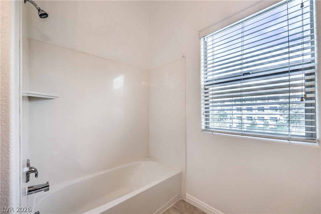 A classic bathtub and shower combination sits adjacent to a large window.