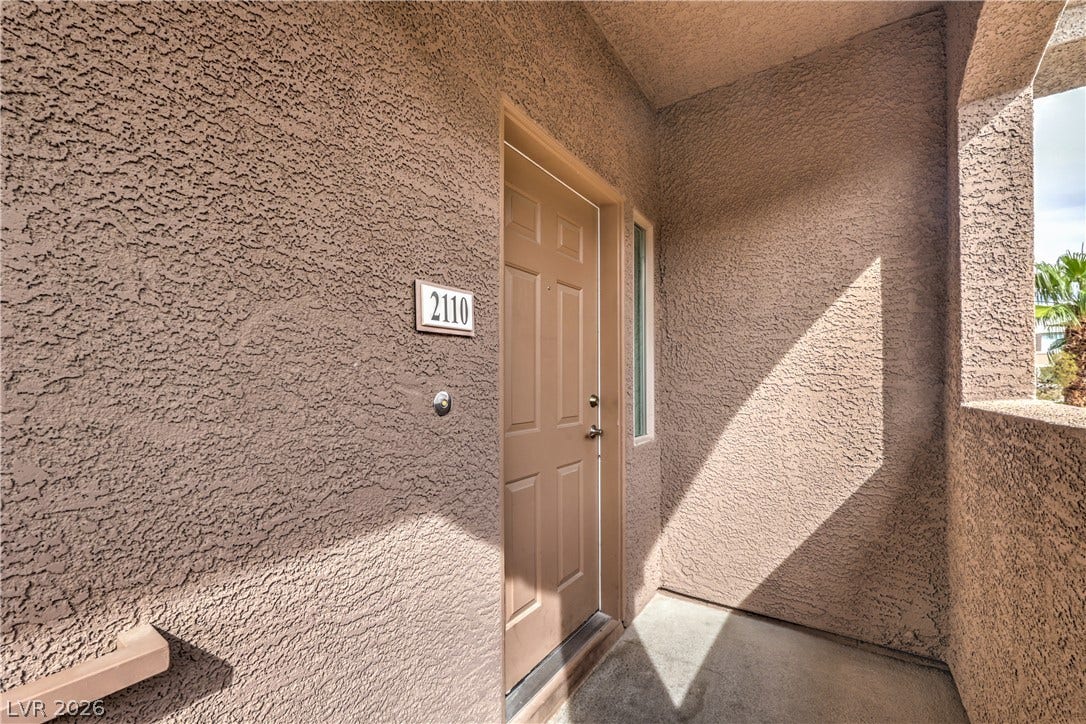 An inviting private entrance features textured stucco walls and concrete flooring.