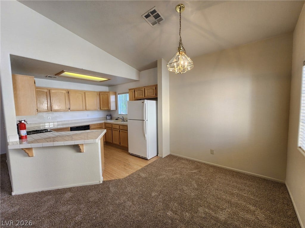 8301 Boseck Drive, #237, Las Vegas, NV 89145 Plush carpeted dining space transitions smoothly into the tile-counter kitchen under vaulted ceilings.
