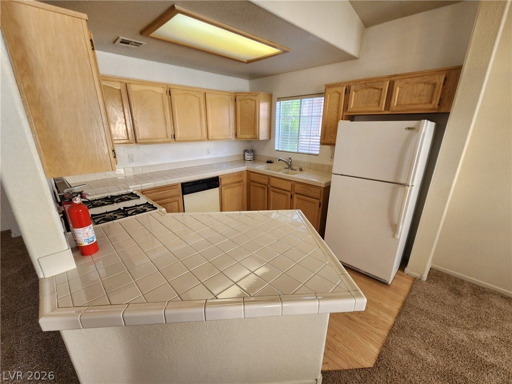 8301 Boseck Drive, #237, Las Vegas, NV 89145 Ample wooden cabinetry and classic tile countertops define this functional, light-filled kitchen space.