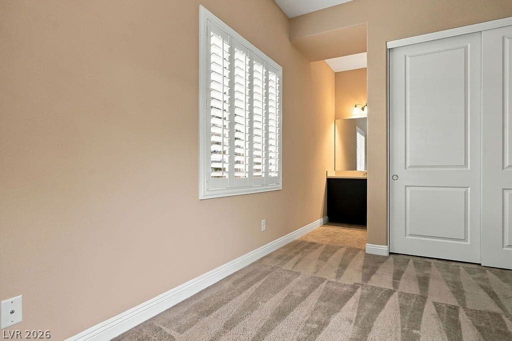 286 Lindura Court, Las Vegas, NV 89138 An inviting bedroom features plush carpeting, classic plantation shutters, and an adjacent bathroom vanity area.