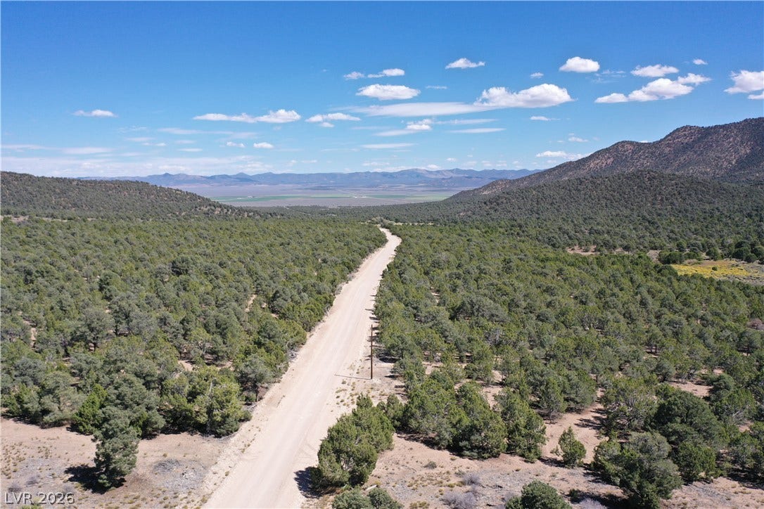 Lot 1-B Side Hill Pass, Pioche, NV 89043 A winding dirt road cuts through vast, tree-covered hills under a bright blue sky.