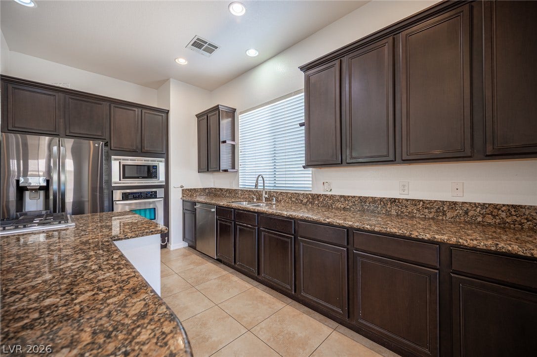 8618 Amber Autumn Street, Las Vegas, NV 89131 Rich granite countertops pair elegantly with dark cabinetry and tiled flooring in this modern kitchen.