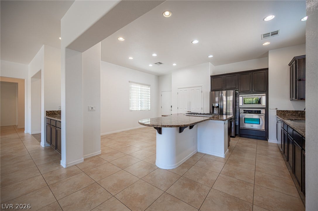 8618 Amber Autumn Street, Las Vegas, NV 89131 Granite countertops and dark cabinetry anchor this open culinary space under recessed lighting.