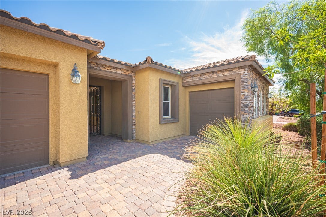 8618 Amber Autumn Street, Las Vegas, NV 89131 Textured stucco and stone accents frame a welcoming paved courtyard entrance with tile roofing.
