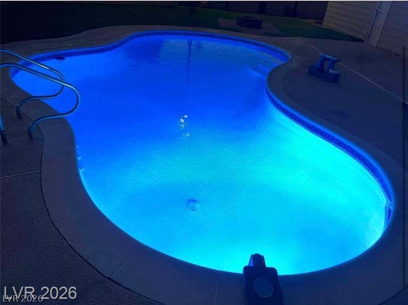 6489 Bugbee Avenue, Las Vegas, NV 89103 A sparkling inground pool glows with vibrant blue light alongside a spacious concrete patio.