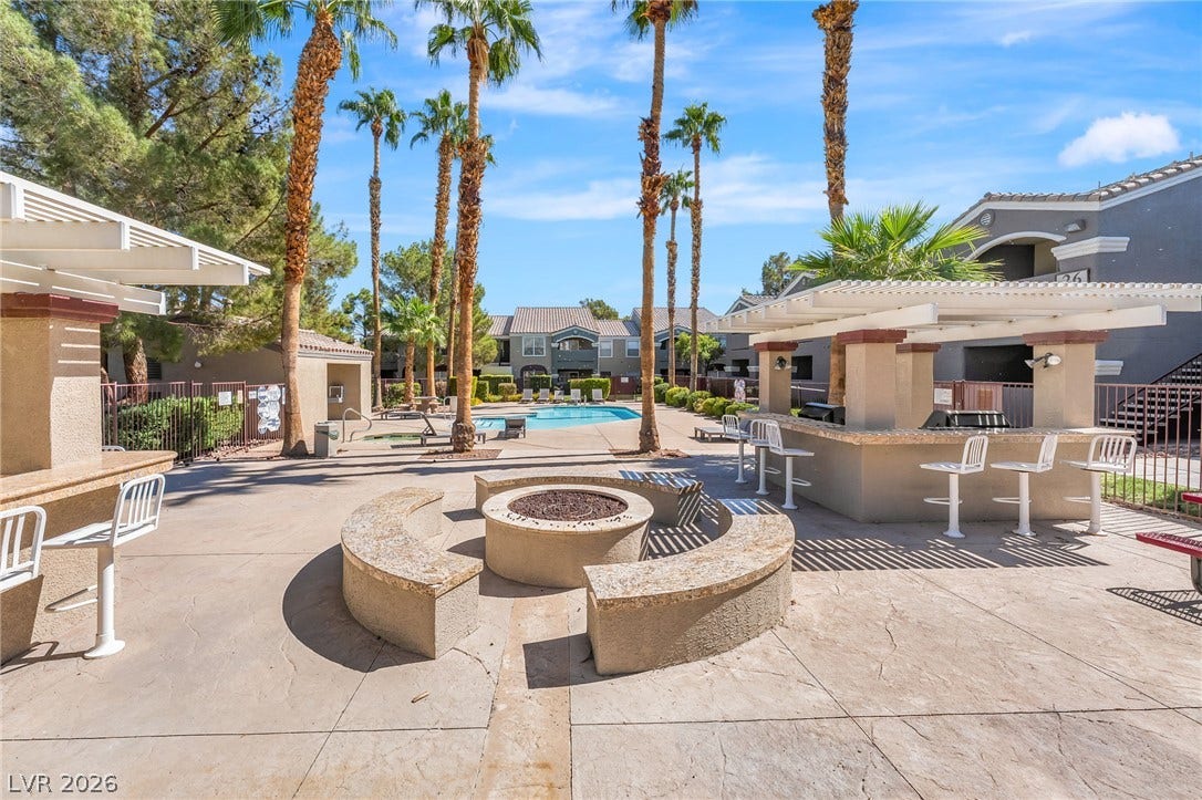 5055 W Hacienda Avenue, #1136, Las Vegas, NV 89118 Palm trees frame a stone fire pit and outdoor kitchen alongside the community pool.