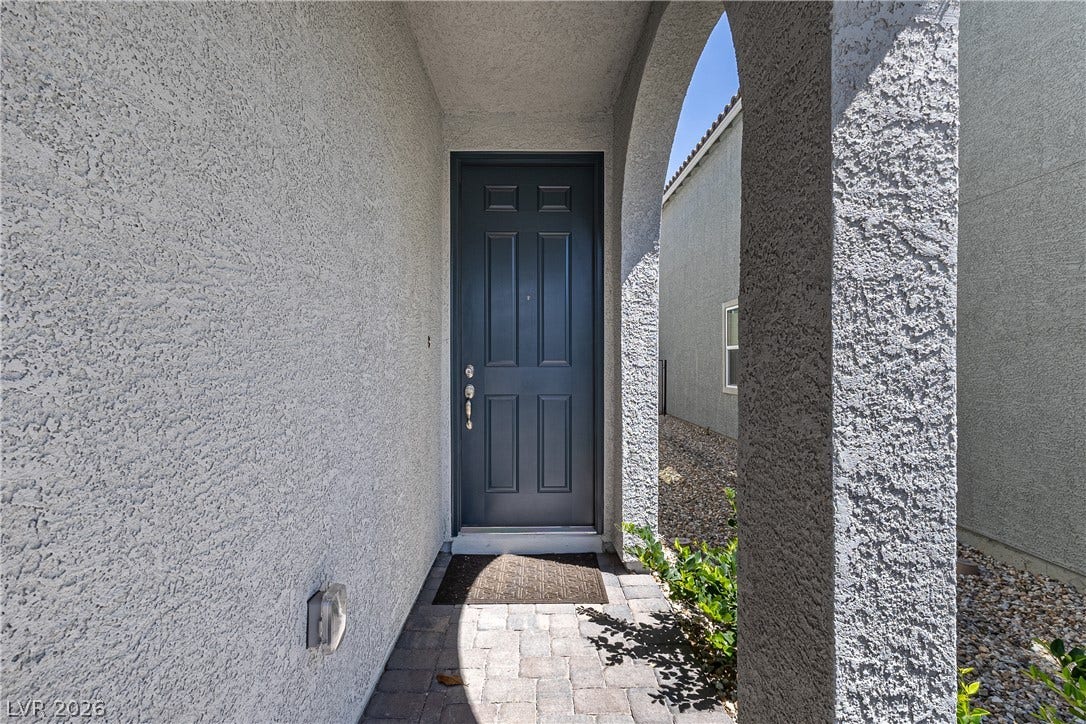 10034 Sir Atlas Court, Las Vegas, NV 89148 An arched stucco entryway with brick pavers leads to a classic paneled front door.
