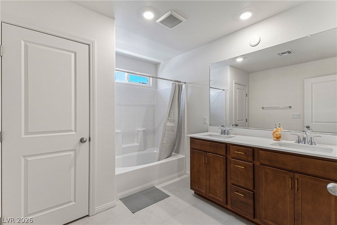 10034 Sir Atlas Court, Las Vegas, NV 89148 Double sinks accent a wood vanity under recessed lighting in this modern bathroom.