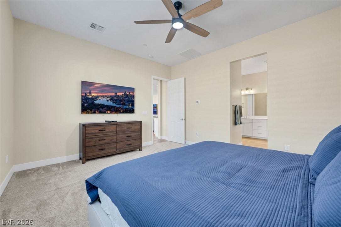 A spacious bedroom retreat boasts neutral walls and soft wall-to-wall carpeting.