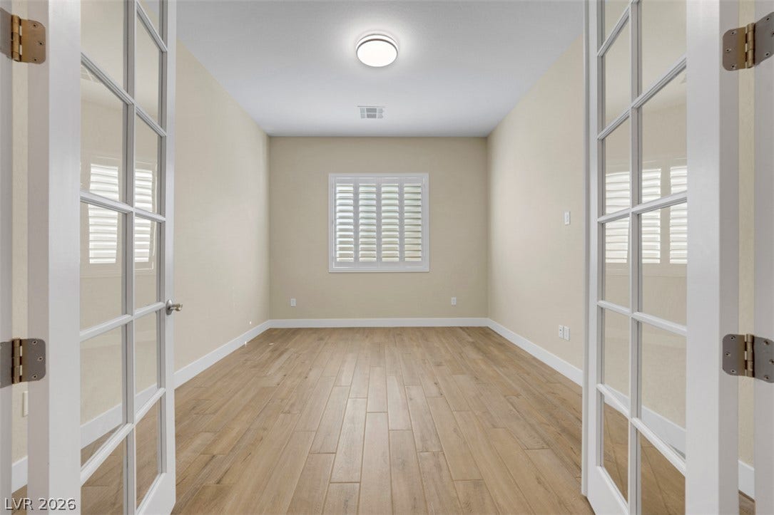 Double French doors open into a versatile home office space with wood flooring.