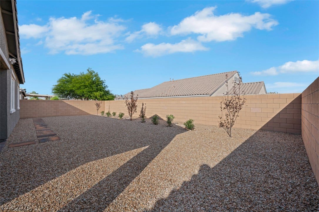 A spacious gravel yard is fully enclosed by secure block fencing under clear blue skies.