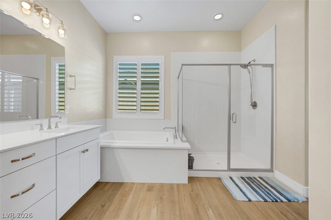 An inviting bathroom displays a modern glass-enclosed shower, a deep soaking tub, and rich wood flooring.