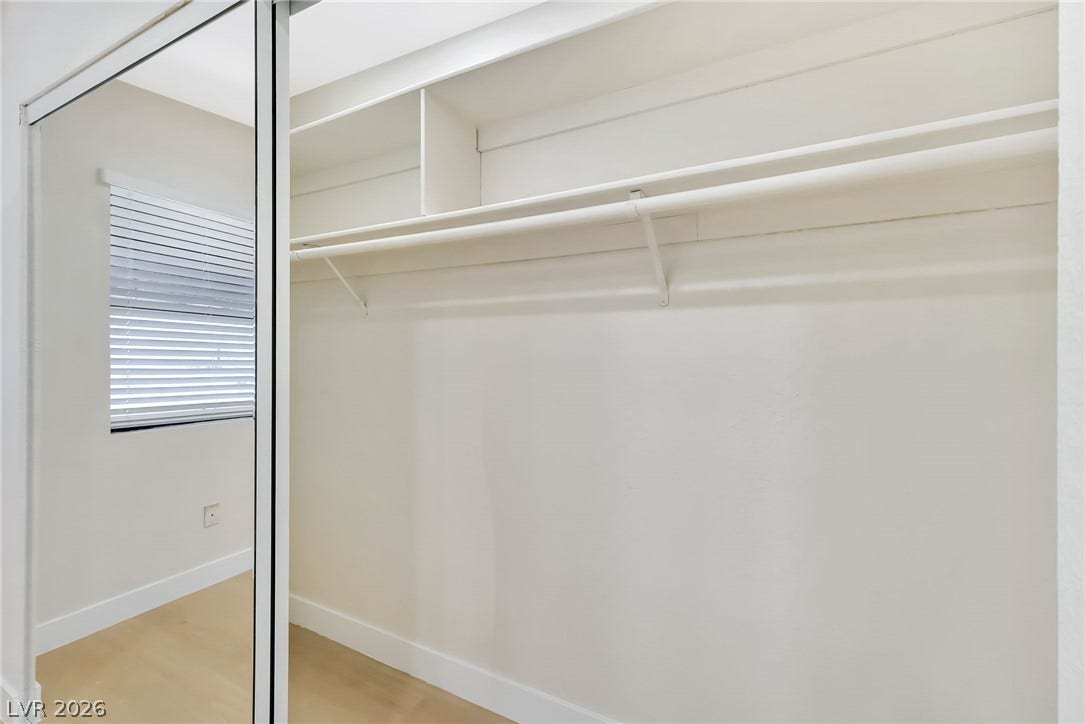 A spacious closet features integrated shelving and mirrored sliding doors alongside light wood flooring.