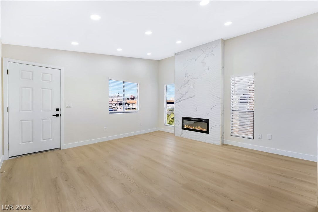 Recessed lighting, smooth flooring, and a floor-to-ceiling fireplace anchor this airy living area.