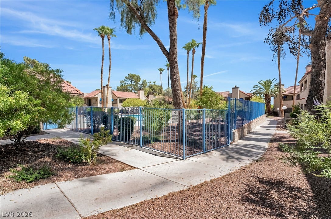 Concrete walkways wind past mature palm trees and fenced recreational facilities under a clear sky.