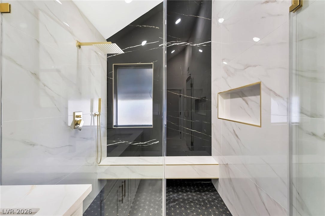 Gleaming marble walls and contrasting geometric tile highlight a contemporary glass-enclosed shower.