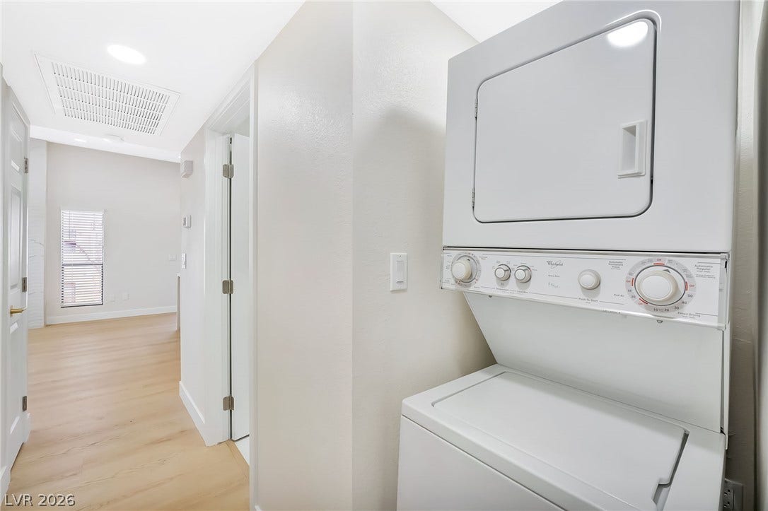 An in-unit stacked washer and dryer setup stands adjacent to light-toned hardwood flooring.