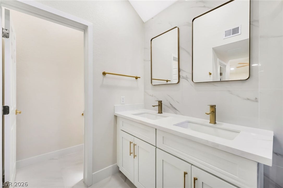 A contemporary vanity setup features dual under-mount sinks and stone counters set against marble-patterned tile.
