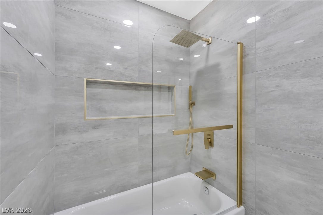 Polished tile surrounds a built-in tub with gold hardware and integrated wall niches.