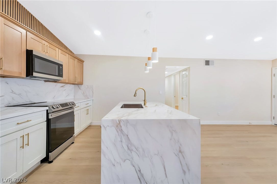 Gleaming marble counters and a matching island highlight this open, wood-floored kitchen area.