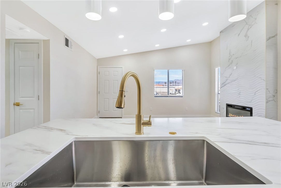 An open kitchen view looks toward a modern living space with a sleek fireplace.