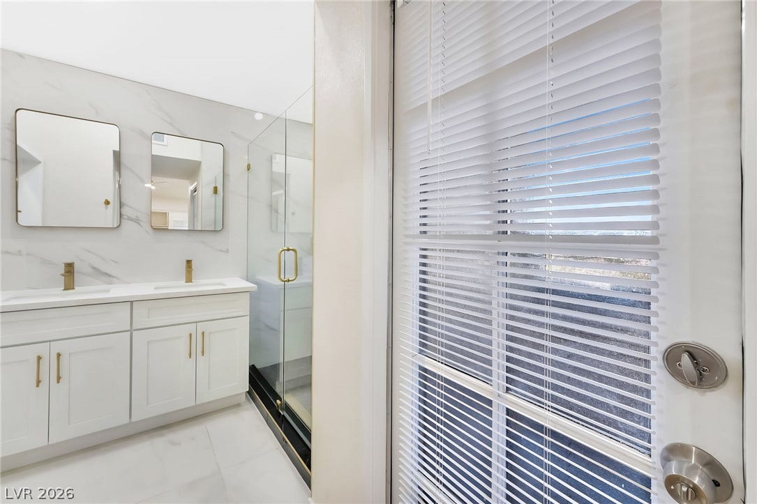 A glass door opens to a bright bathroom with stone-patterned walls and marble floors.