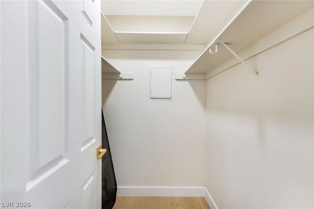An organized closet provides built-in wooden shelving over light hardwood flooring.