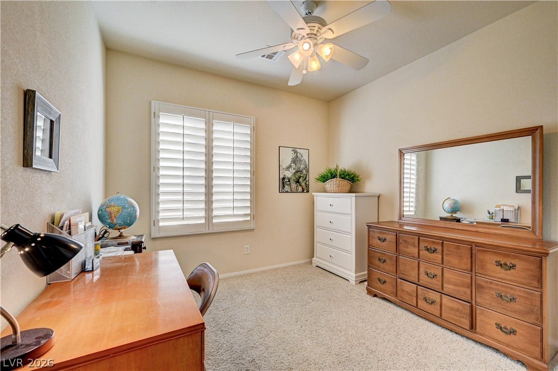 A spacious secondary bedroom features neutral carpeting and a large window with plantation shutters.