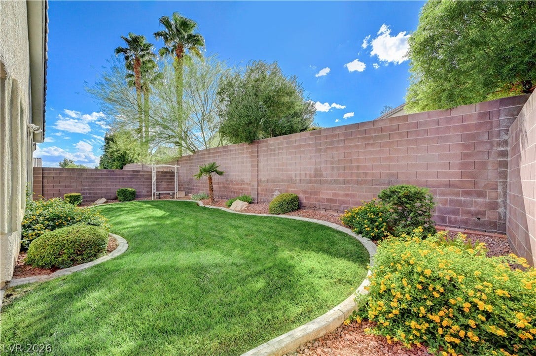 A curved green lawn is enclosed by high privacy block walls under blue skies.