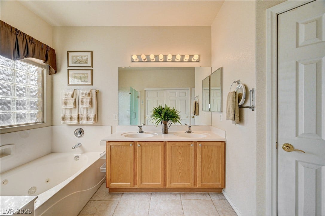 An inviting soaking tub pairs beautifully with a spacious double vanity and tiled flooring.