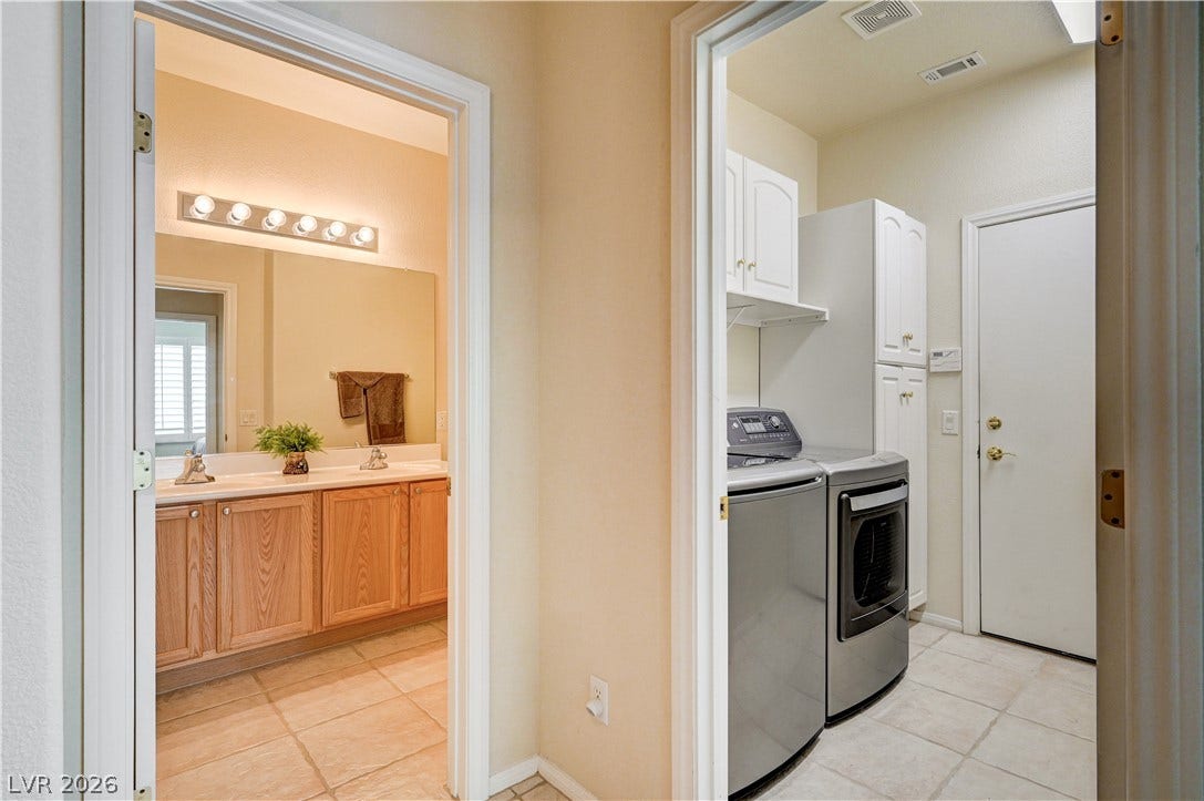 Tiled flooring connects a practical laundry room to an adjacent bathroom vanity area.