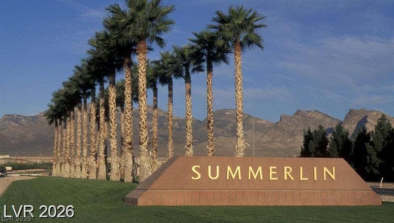 Towering palm trees frame the community entrance sign set against a rugged mountain backdrop.