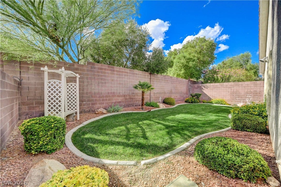 Manicured green lawn and mature plantings line this private, brick-walled backyard sanctuary.
