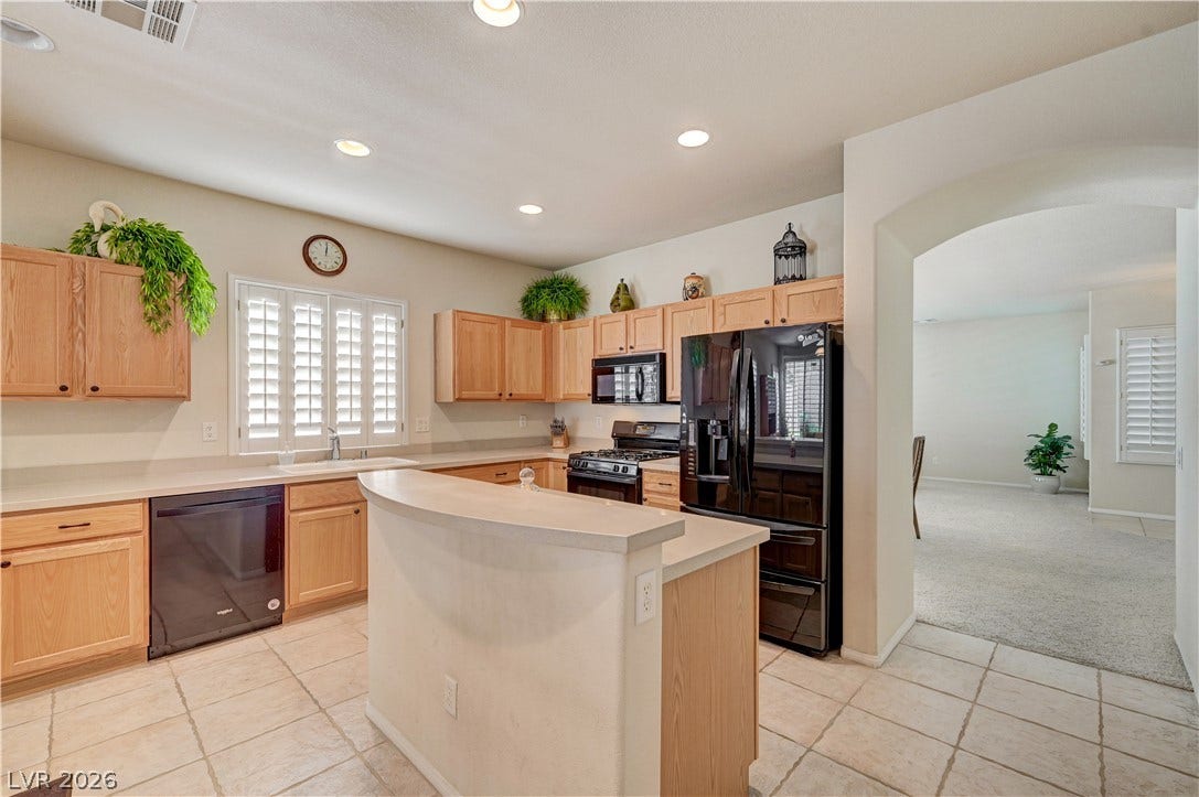 An arched doorway connects the tiled kitchen and carpeted living areas in this open layout.