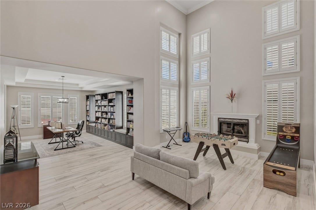 Double-height ceilings and tall shuttered windows frame this open, light-filled living area.