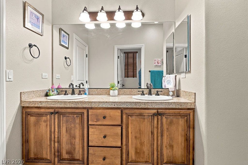 A spacious double vanity offers ample wooden cabinetry and stone countertops in this bathroom.