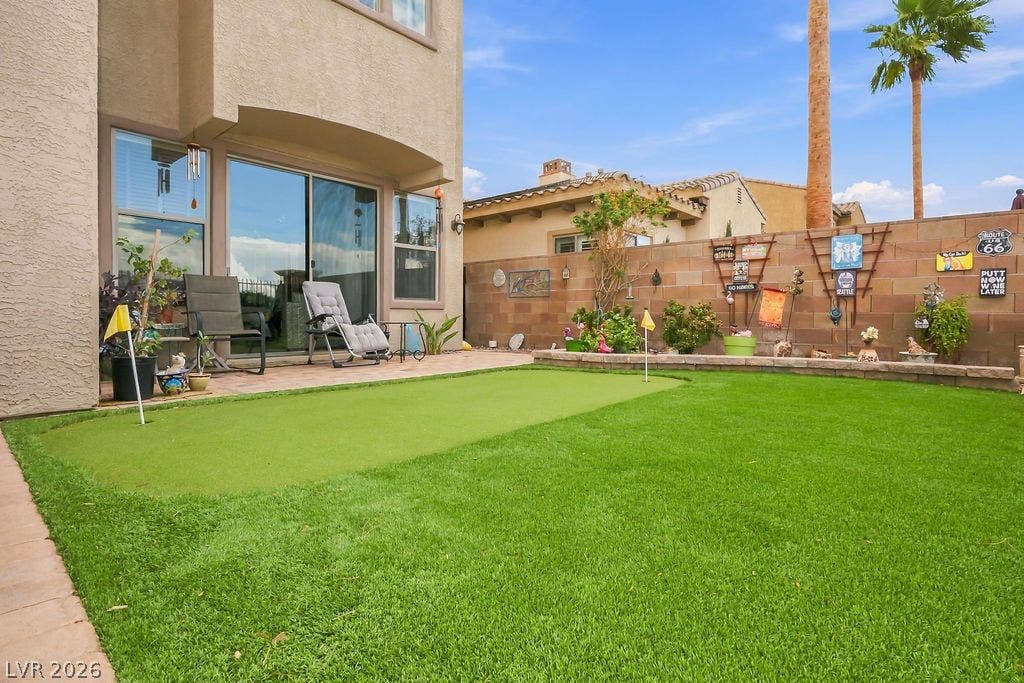 An inviting backyard features a pristine putting green alongside a paved patio area.