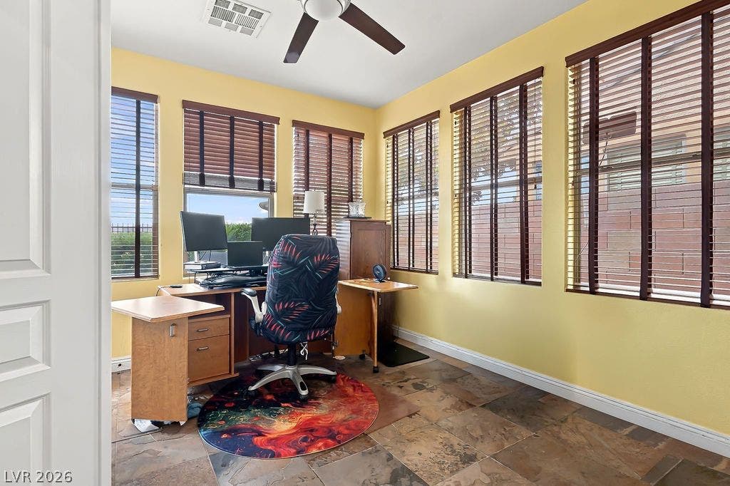 Natural light floods this versatile home office through numerous windows over durable tile flooring.