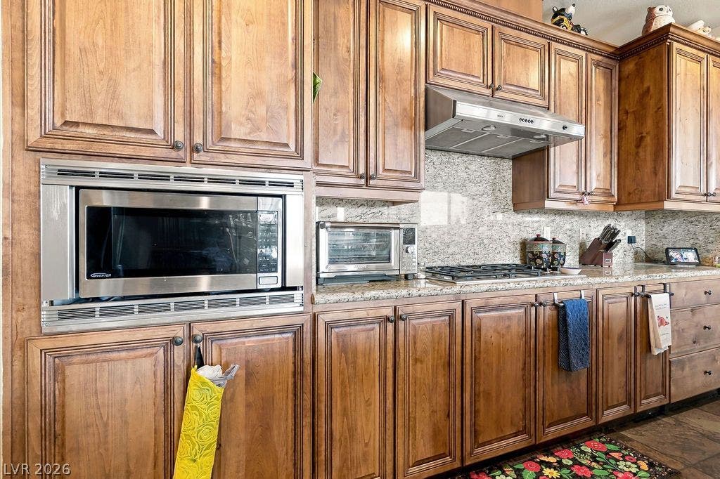 Rich wood cabinetry surrounds integrated stainless steel appliances and polished stone countertops.